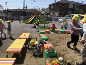晴天の中、沢山の子ども達が砂場や園庭で楽しそうに遊んでいる。