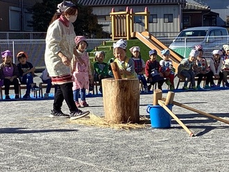 お餅つきをする子どもと見守る保育士の写真