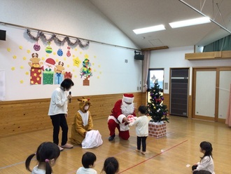 クリスマス会でサンタクロースからプレゼントをもらう子ども達の写真