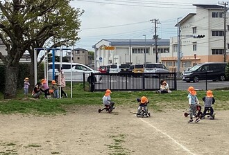 保育所の園庭で子ども達が虫探しや三輪車に乗って遊んでいる写真