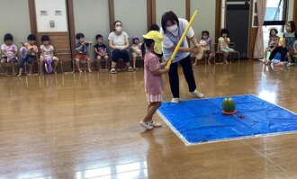 ホールで3、4、5歳児がすいか割りをしている写真