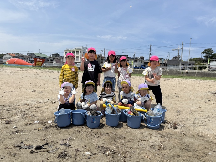 海で拾ったごみが入ったバケツを前にみんなで並んで写真を撮る