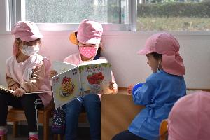 写真：図書館で3人の園児が本を読んでいる
