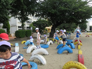 写真：校庭でタイヤの遊具の上に乗って楽しむ年長さん