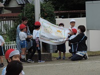 写真：幼稚園の園旗ができ、掲揚塔に取り付けている様子