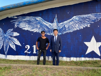 写真：阿字ヶ浦ミューラルプロジェクトの壁画作品を前に記念撮影をするtwoone氏と大谷市長