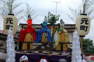 写真：白い顔、青い顔、赤い顔の3体のみろく人形が乗る屋台