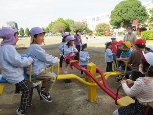 写真：小学校の中庭で1年生と一緒にシーソーを楽しむ年長児