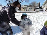 写真:年少児が先生と一緒に雪だるまを作っている