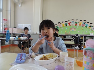 写真：笑顔でカレーのお弁当を食べている年長女児