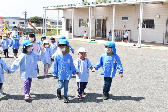 年長さんが年中さんの手を引いて園庭を歩いている