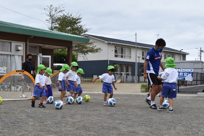 年中組の園児とサッカーのコーチがボールを蹴っている。