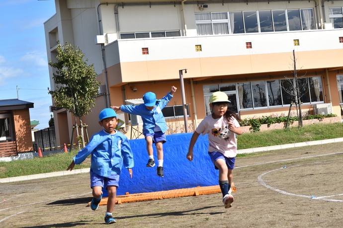 大きなマットを飛び越えて走る園児