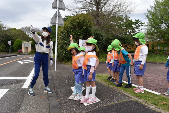 向かい側を指さす指導員と道路を渡ろうとする園児