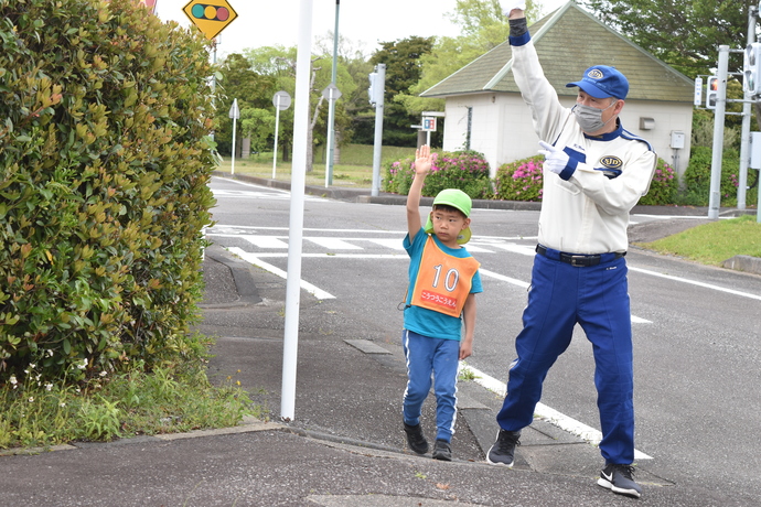 垣根の脇の道路を渡る園児と指導員