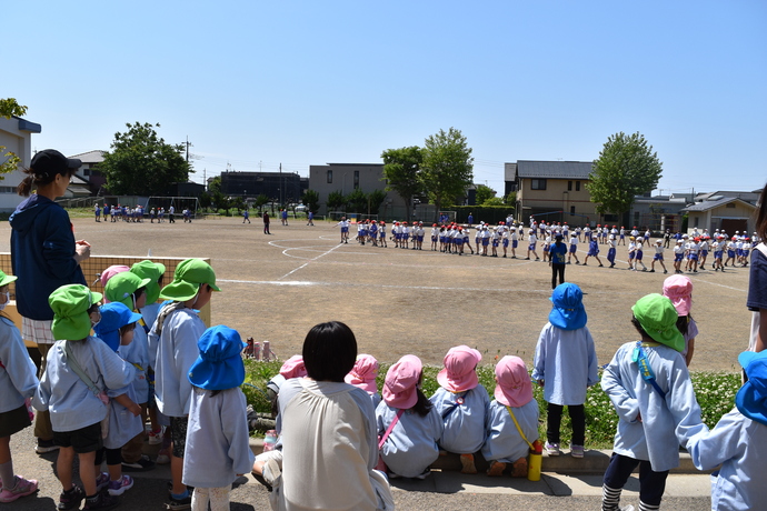 校庭で小学生のダンスを見る園児