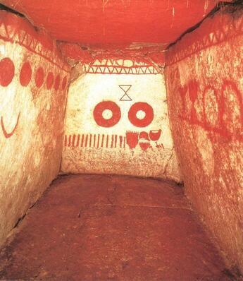 虎塚古墳石室内を入口側から撮影した写真。白い壁に赤い装飾が施されている。正面には、虎塚古墳の象徴的な図形、三角形2つを頂点が1つずつ接した図形の下に、ドーナツ型の赤い丸が2つ並んで描かれている。天井は全て赤く、左右の壁には正面とは違う様々な図形が描かれている。